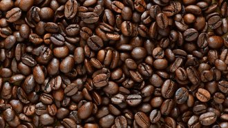 Detailansicht in Draufsicht von dunkelbraunen, gerösteten Kaffeebohnen, die wild übereinander liegen – eventuell in einem Kaffeesack. Das Bild repräsentiert den Fachbereich KAFFEE & GENUSS der offino Bürolösungen GmbH.