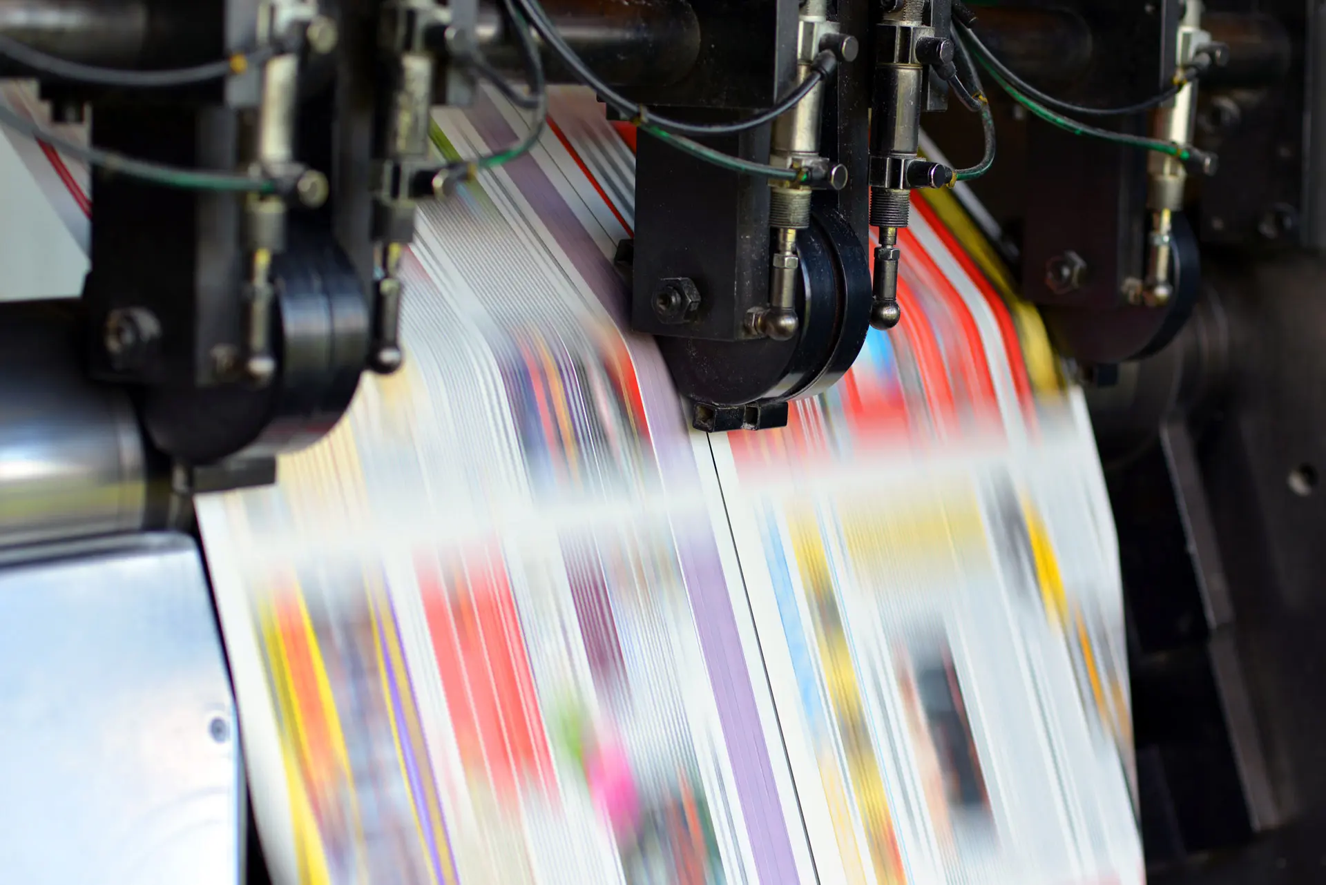 Detailaufnahme des Ausgabefach einer Druckmaschine der offino Bürolösungen GmbH – aufgrund der Bewegungsunschärfe sind die ausgegebenen Druckprodukte eines Kunden lediglich als dynamische, leicht unscharfe Farbschlieren zu erkennen.