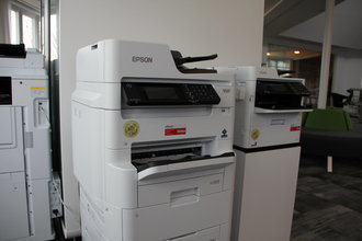 Blick auf zwei nebeneinander stehenden EPSON-Druckern vor einer weißen Bürowand