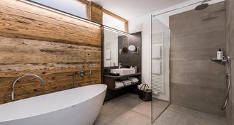 Modernes Badezimmer teilweise in Holz-Look mit einer Badewanne, einem Bereich für die Dusche und ein Waschbecken vor einer Spiegelwand