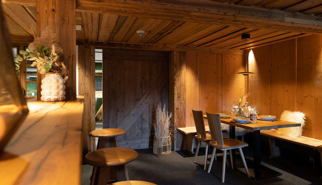 Dunkles und gemütliches Restaurant mit Holz-Ästhetik. Zu sehen ist eine hölzerne Schiebetür, davor befinden sich gedeckte Esstische mit Stühlen.
