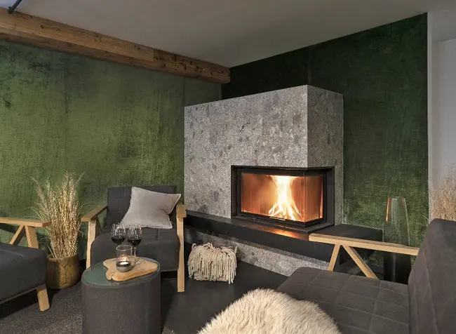 Gästeraum mit modernem Kamin. Vor dem Kamin befinden sich gemütlich Stühle, die um einen kleinen Tisch platziert sind.